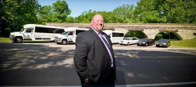 A man in a suit standing in front of the white limo coaches and limousines of the fleet