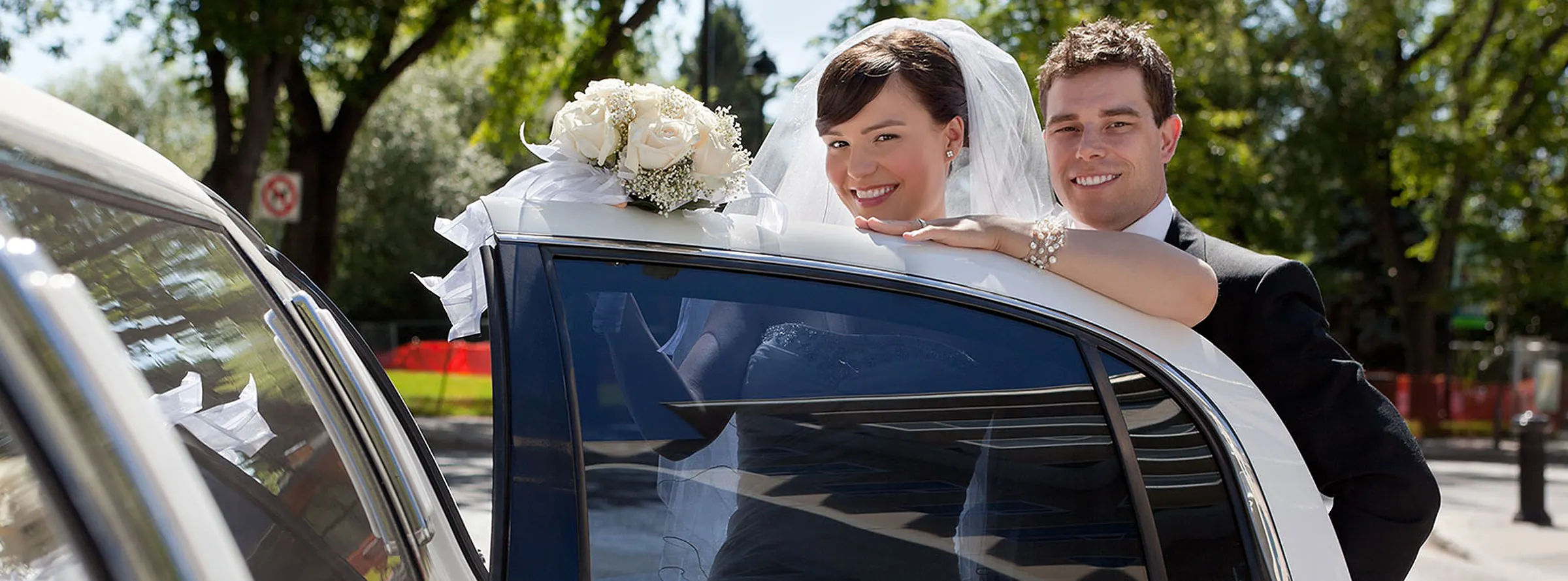 A smiling bride and groom leaning on the open door of a white limousine