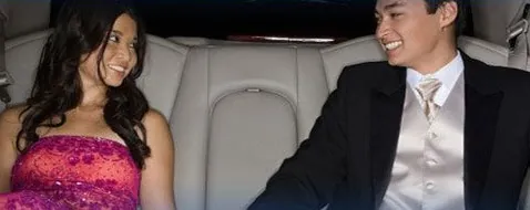 A prom couple seated in a white leather limousine