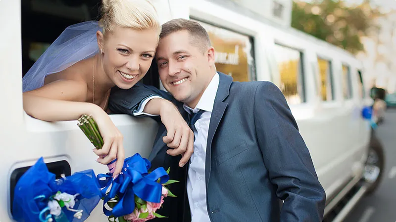 A smiling bride and groom leaning out of a white limousine