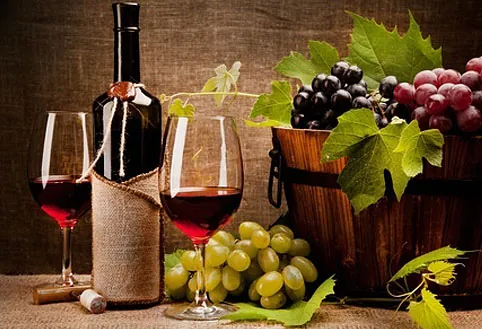 Red wine, a wine bottle and bunches of grapes on a rustic table