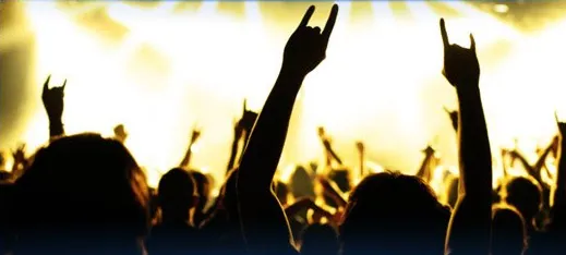 A concert crowd with hands raised under stage lights
