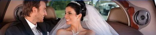 A bride and groom smiling at each other in the back of a limousine